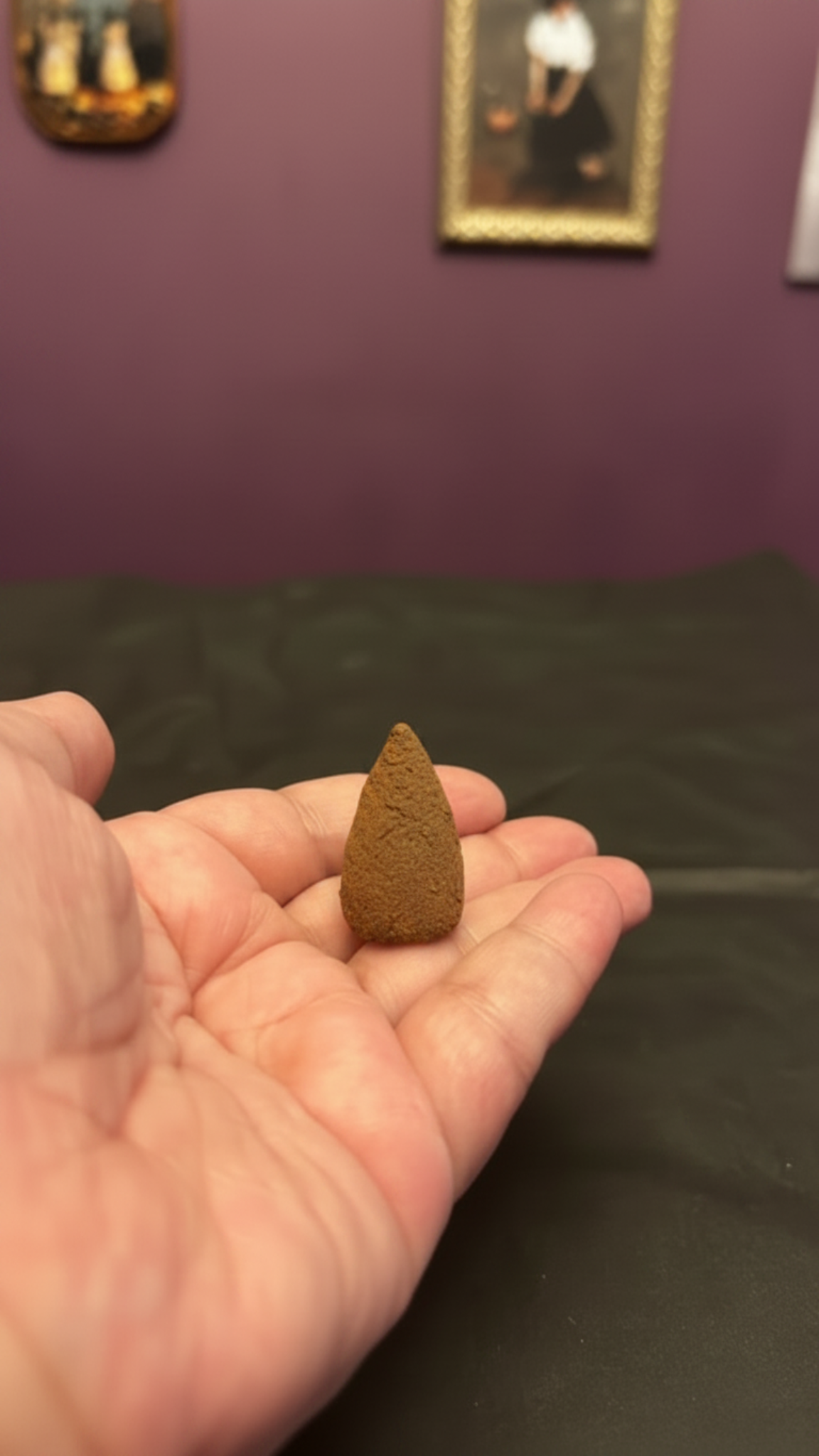 Single brown, textured incense cone resting in an open palm.